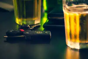 Car keys and glass with beer or alcoholic beverage in a bar, which often leads to needing a DUI lawyer.