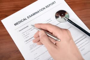 Image of doctor filling out blank Medical Examination Report form with respect to light duty work after a work injury.